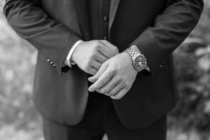 Close-up of formal black suit jackets and hands at wedding ceremony.