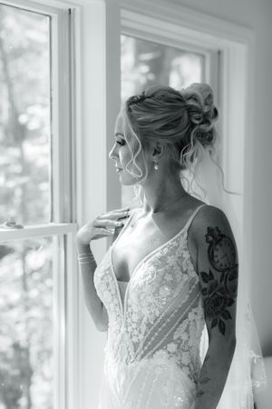 Bride in lace wedding dress gazing through sunlit window.