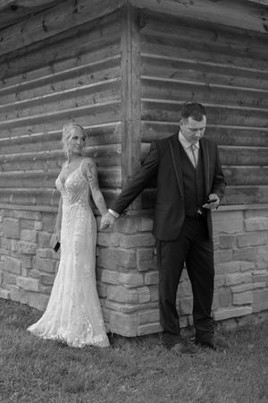 Couple poses against rustic log cabin wall for wedding photos.