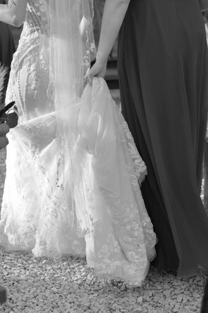 Detail shot of wedding dress train and formal shoes on gravel path.