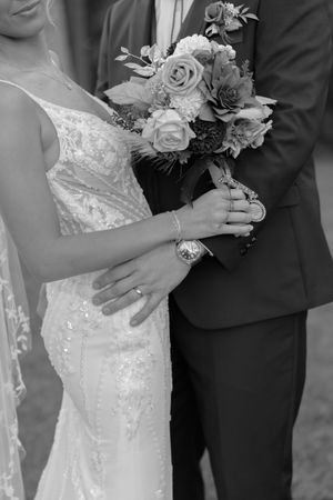 Wedding couple holds bouquet of white roses and flowers in black and white photograph.