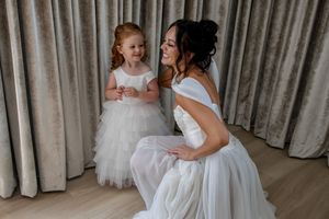 People in white dresses share tender moment in room with curtained backdrop.