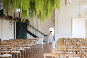 Wedding venue with hanging greenery and rows of wooden cross-back chairs set up for ceremony.