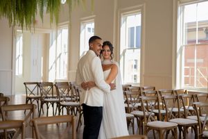 Bright wedding venue with natural light streaming through windows and cross-back chairs in rows.
