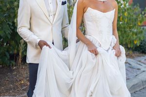 Wedding couple in coordinating white formal wear stand close together on outdoor stone paving.