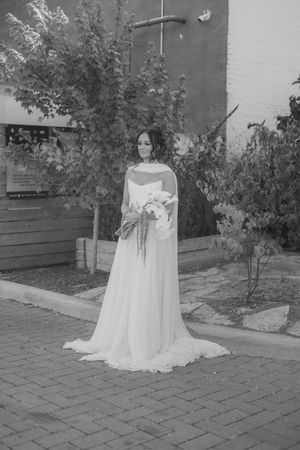 Black and white wedding photo of a person in a flowing white gown standing on brick pavers.