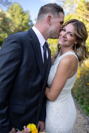 Newlyweds share intimate moment in formal attire with sunlit garden backdrop.
