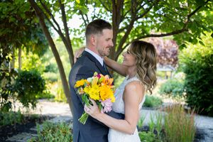 Wedding couple shares romantic moment in garden setting with bright yellow bouquet.