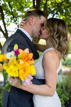 Bride holding colorful bouquet embraces groom in garden setting.