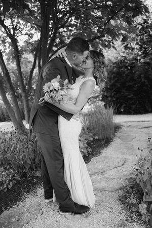 Black and white photo of wedding couple sharing intimate moment on garden path.