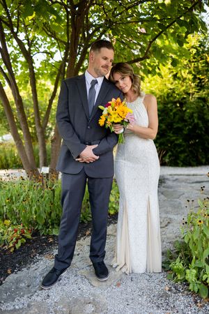 Newlyweds share intimate moments along a gravel path with vibrant yellow sunflower bouquet.