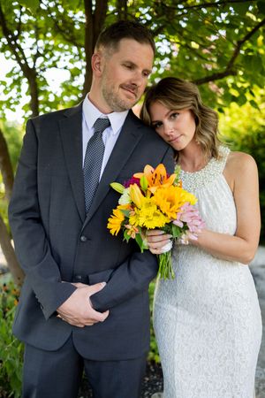 Wedding couple poses in garden setting with sunflowers and white lace dress against natural backdrop.