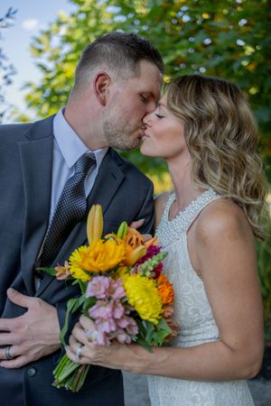 Romantic wedding couple shares intimate kiss while holding vibrant sunflower bouquet.