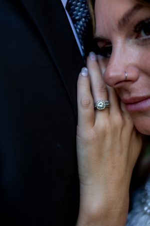 Close up of sparkling engagement ring on bride's hand against dark background.