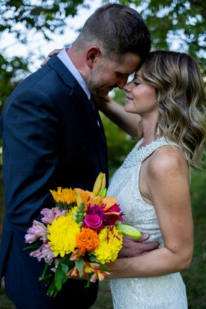 Wedding couple kisses while bride holds vibrant yellow and pink bouquet outdoors.