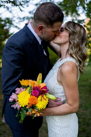 Tender wedding moment captured with bright floral bouquet against natural backdrop.