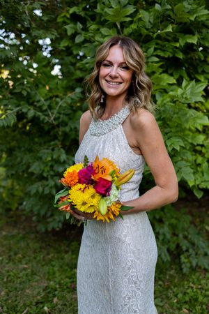 Joyful bride poses with vibrant summer bouquet in outdoor garden setting.