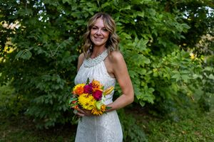 Elegant bride with wavy hair holds bright floral bouquet in garden setting.