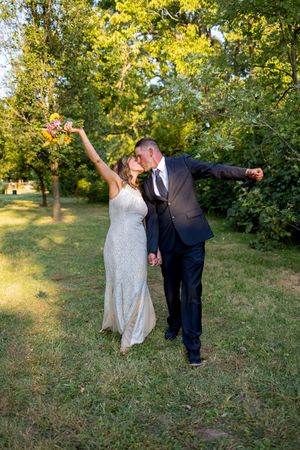 Playful wedding couple dances and celebrates in sunlit garden setting.