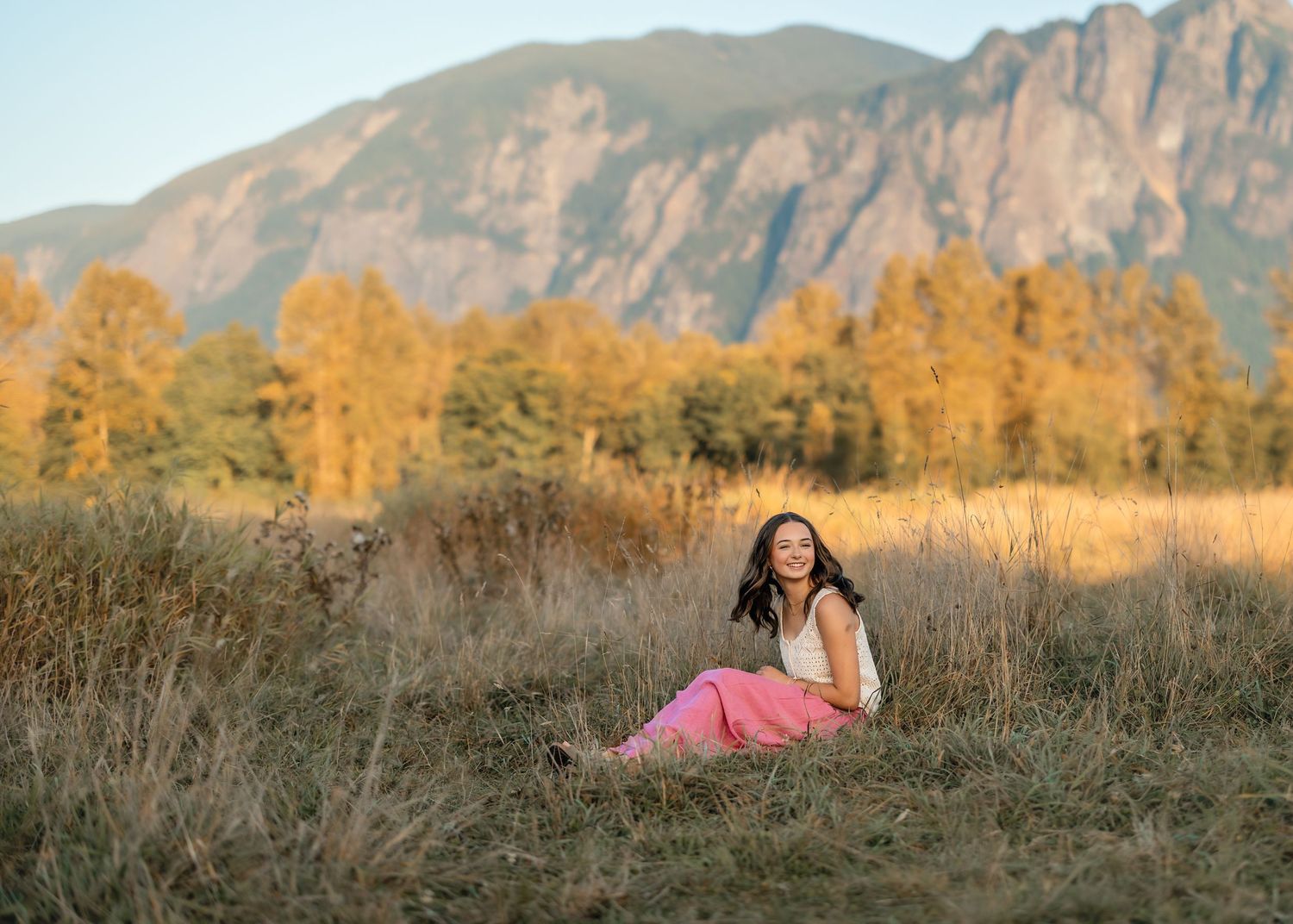 Golden autumn grass field with rocky mountain peaks in background at sunset.