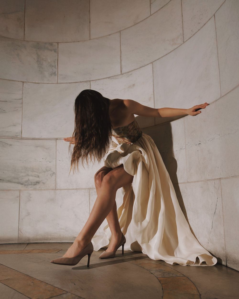 A series of images showing someone crouched on the floor in a white dress and heels against a curved wall.