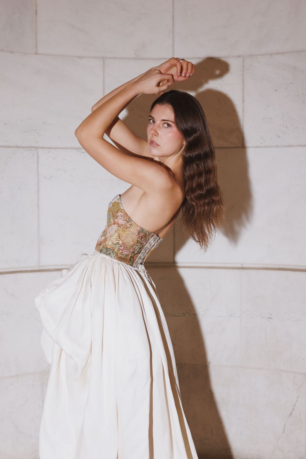 A flowing white dress photographed in sequence against light stone wall backdrop.