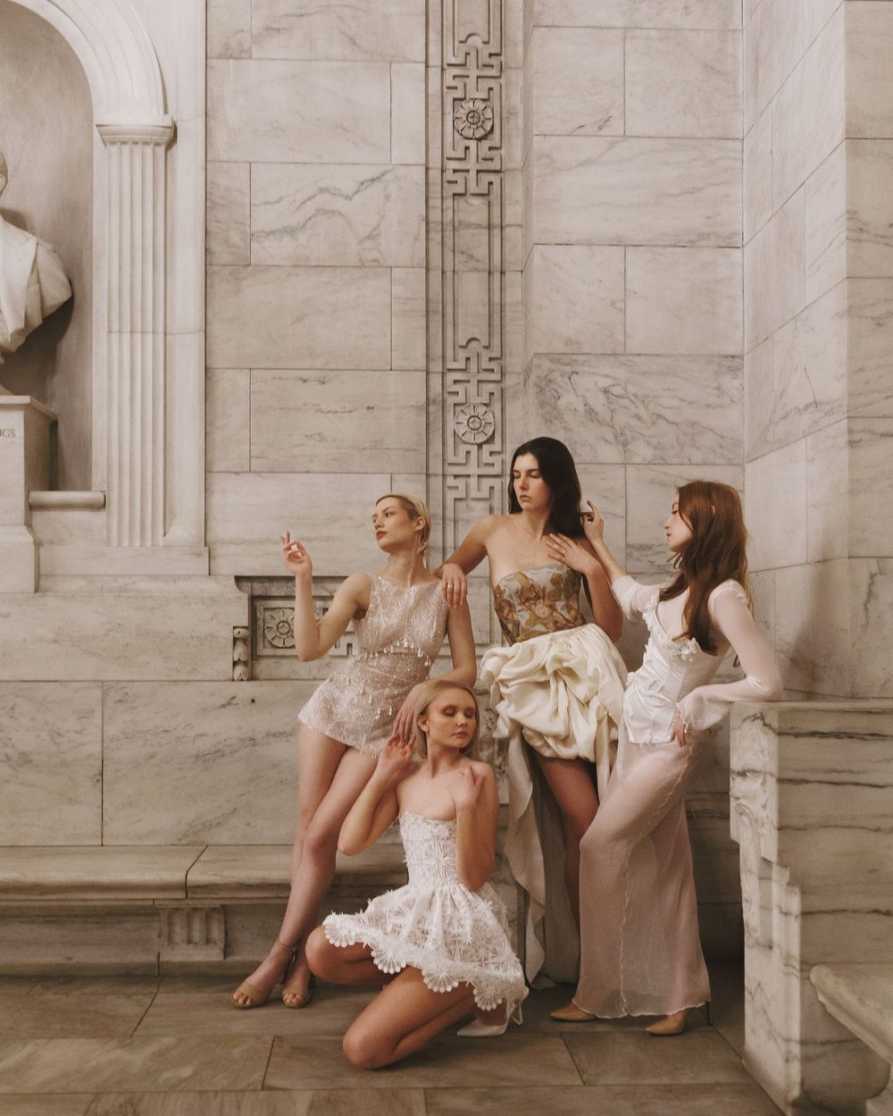 Bride and bridesmaids in white dresses pose playfully between marble columns at an elegant venue.