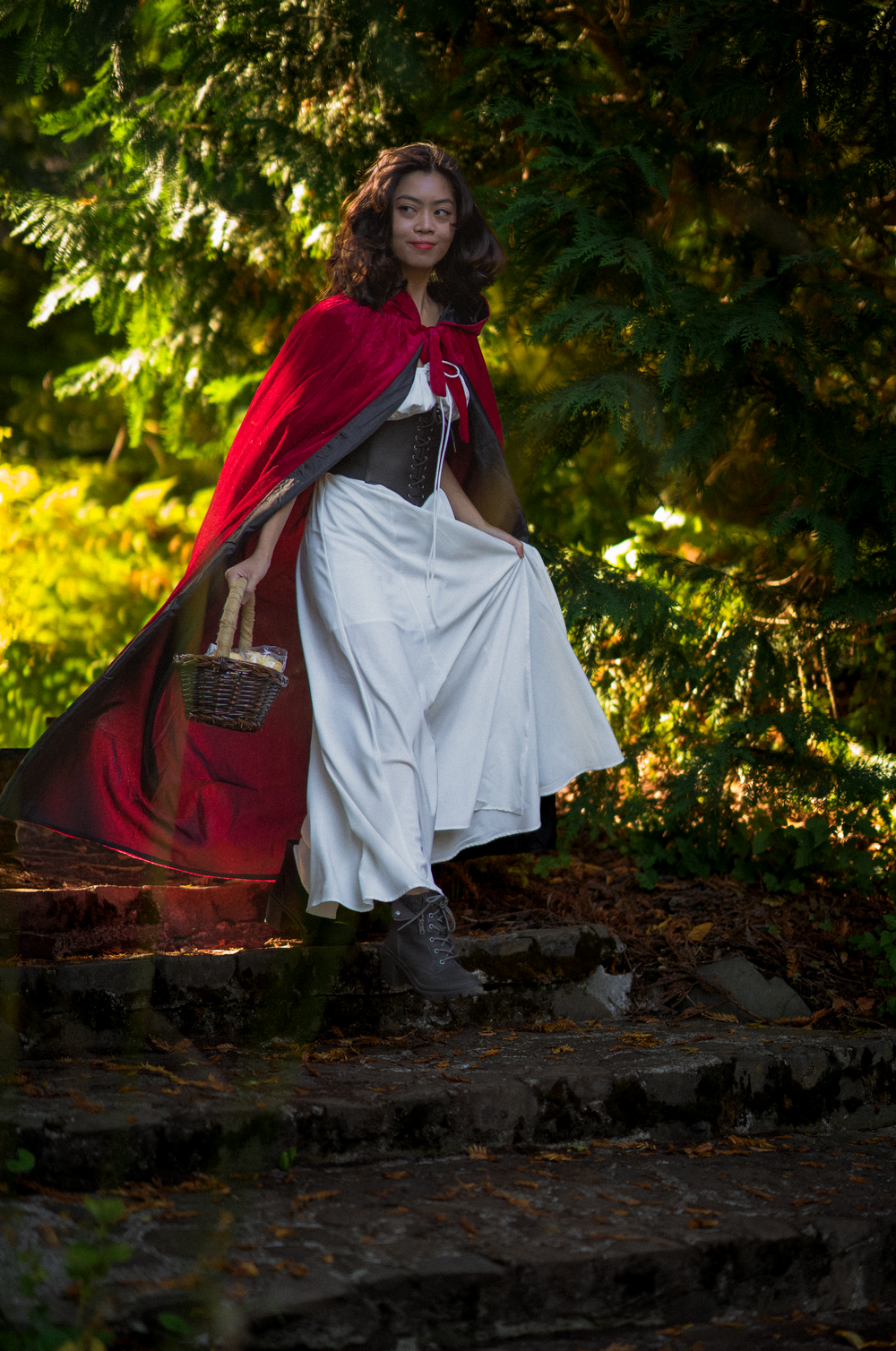 A figure in red and white clothing sits on stone steps in a sunlit wooded area.