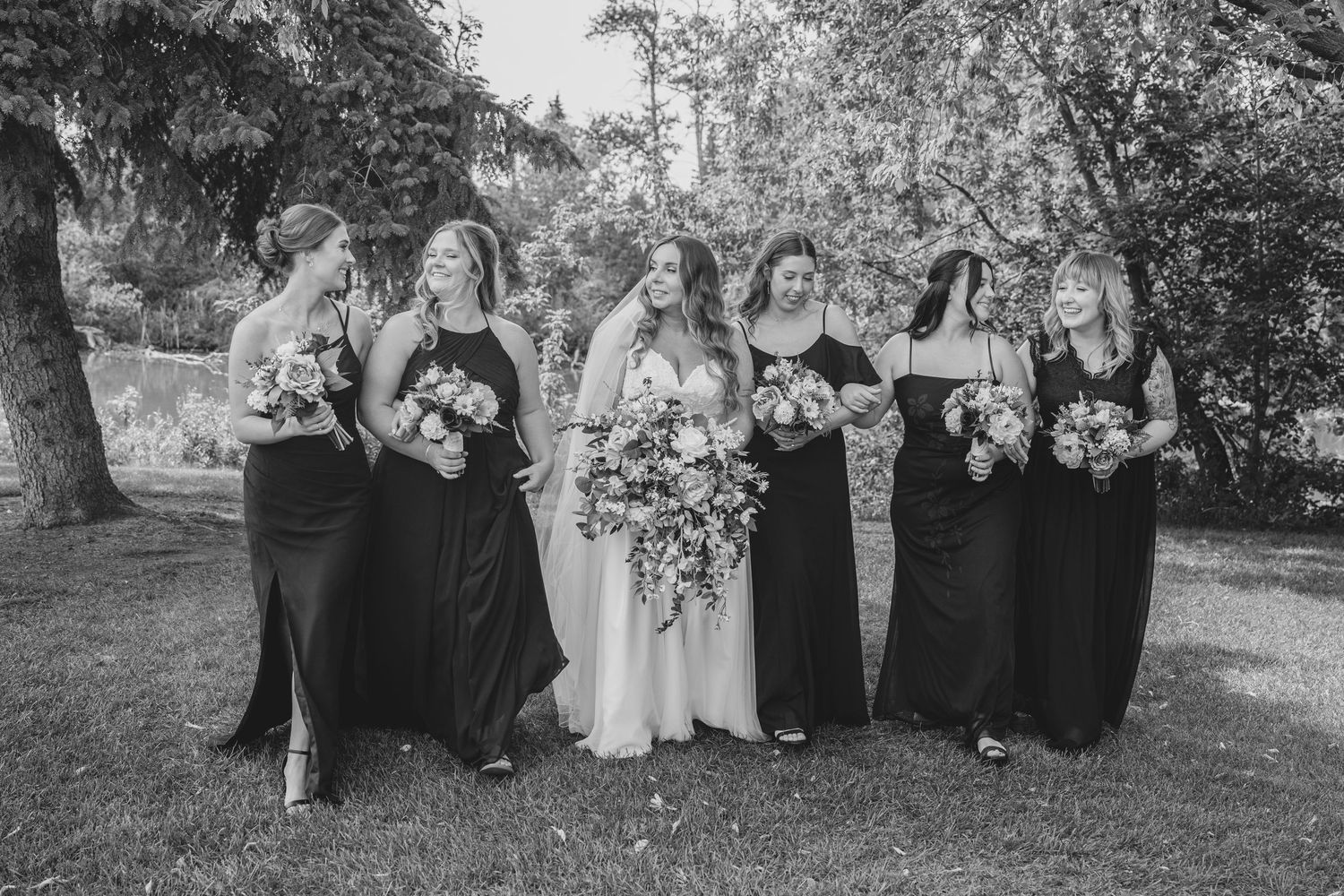 Wedding party poses together outdoors in garden setting wearing black and white formal attire against natural backdrop.