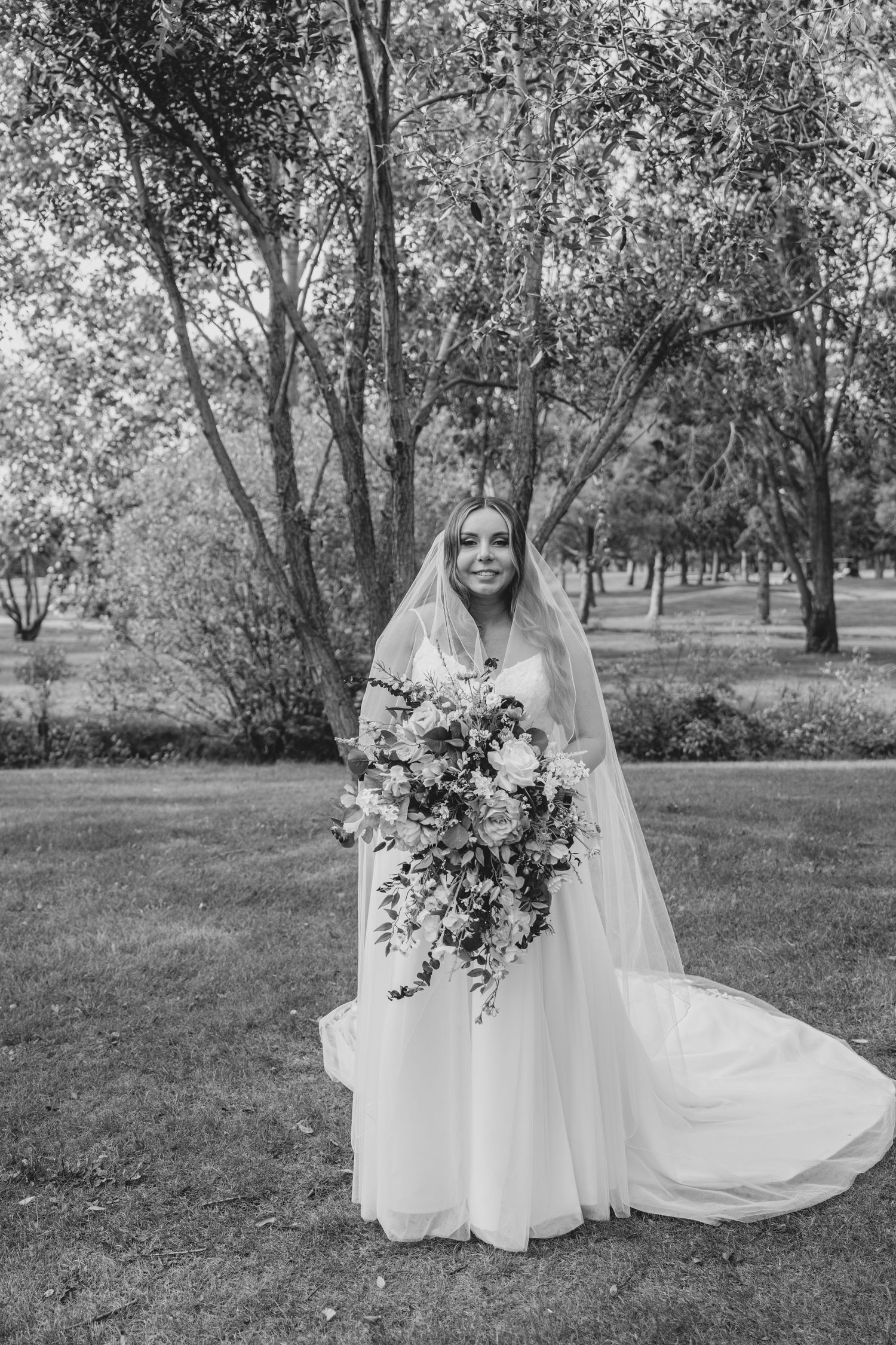 Black and white collage of bride in flowing gown and veil posing gracefully in an outdoor garden setting with trees.