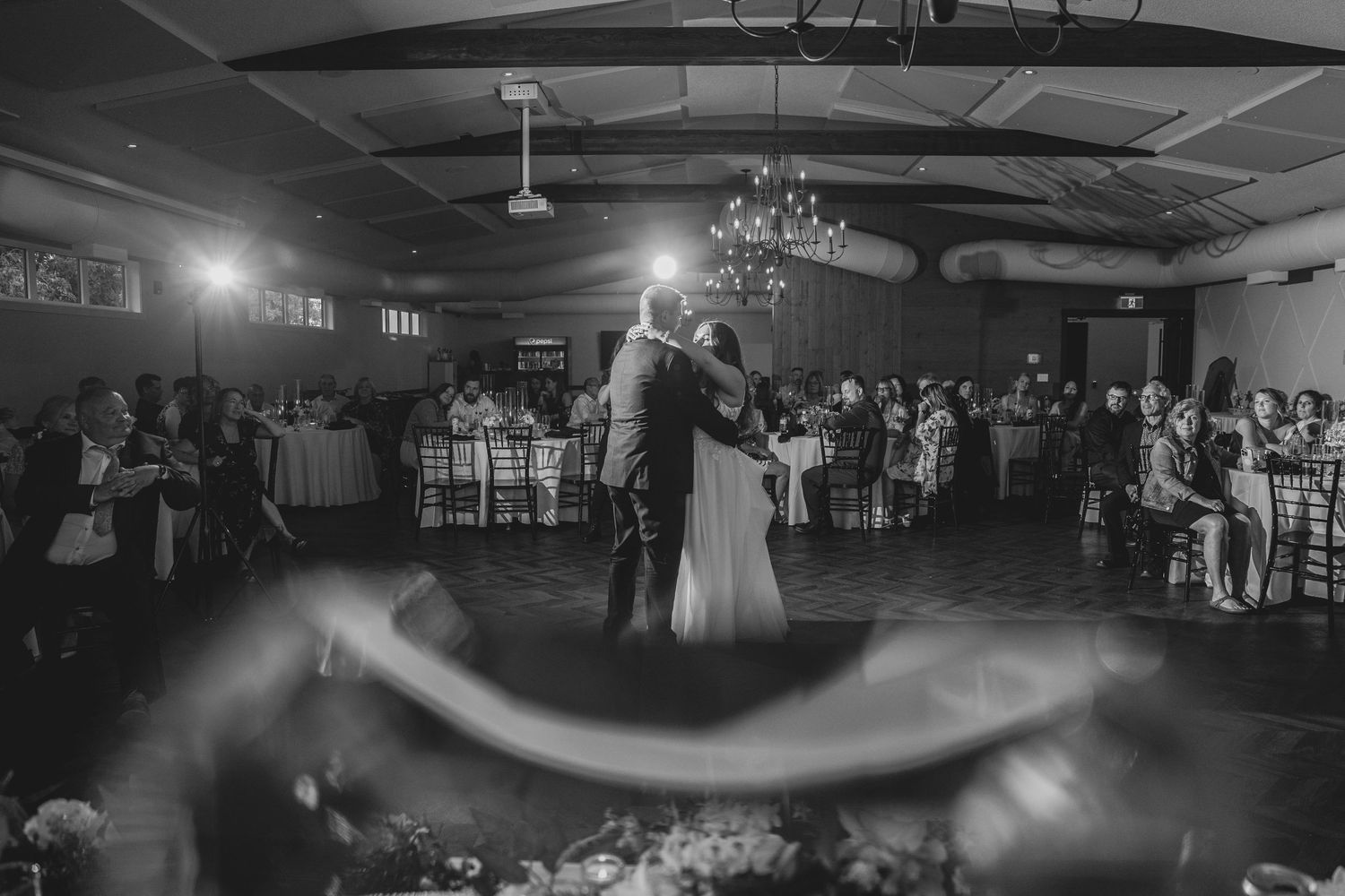 Black and white panoramic view of a wedding reception dance floor with dramatic lighting effects.