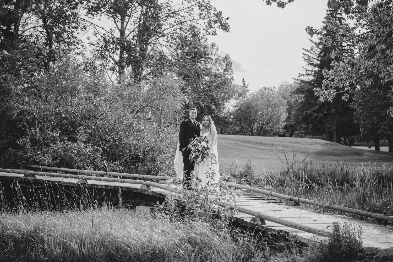 Newlyweds share a romantic moment on a rustic wooden bridge in a natural setting.