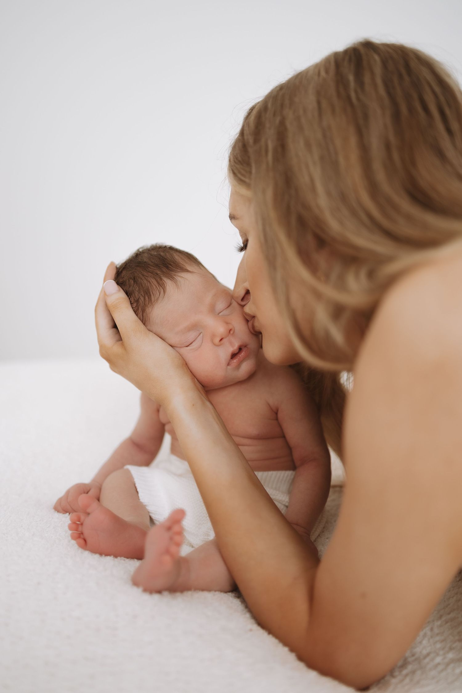 A baby lies on white bedding while a caregiver gently touches their tiny feet in a tender moment.