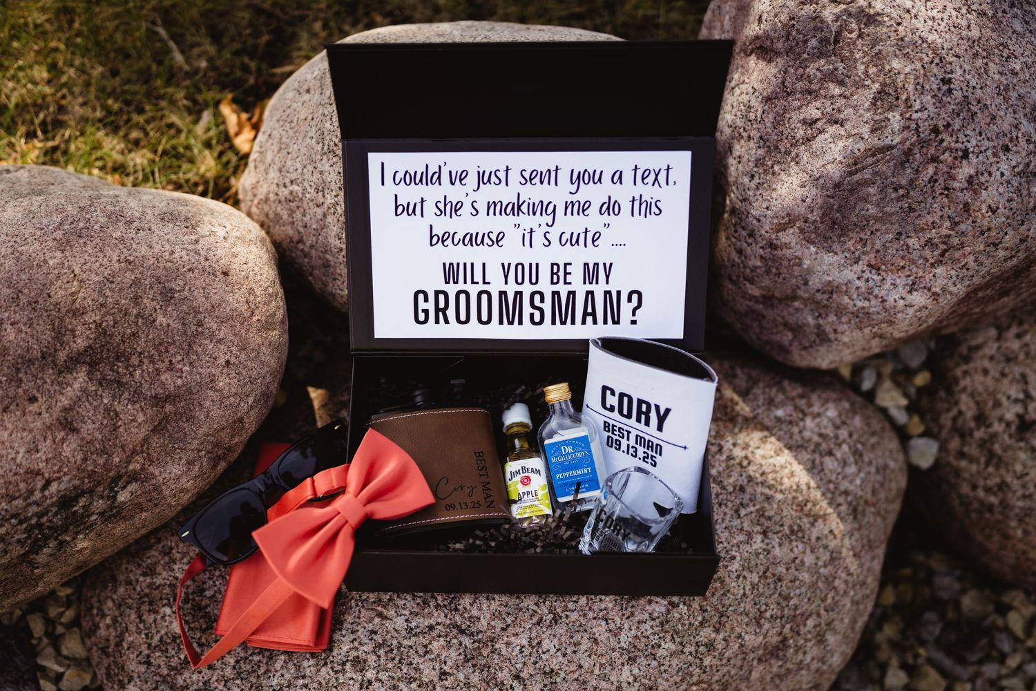 A creative groomsman proposal decorative display arranged on rocks with red bowties and message cards.