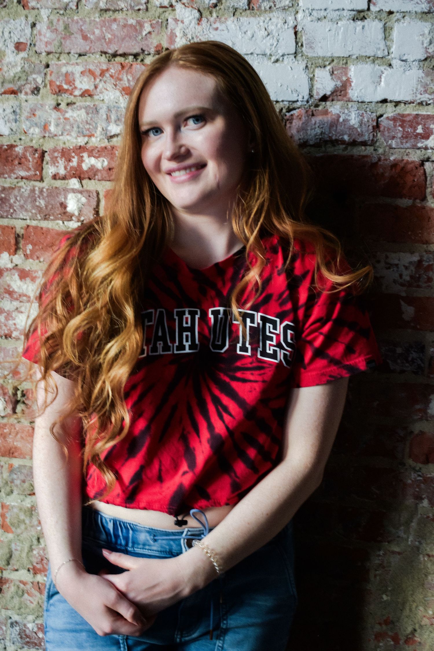 High school senior girl in casual jeans and t-shirt leaning on a brick wall in Seattle.