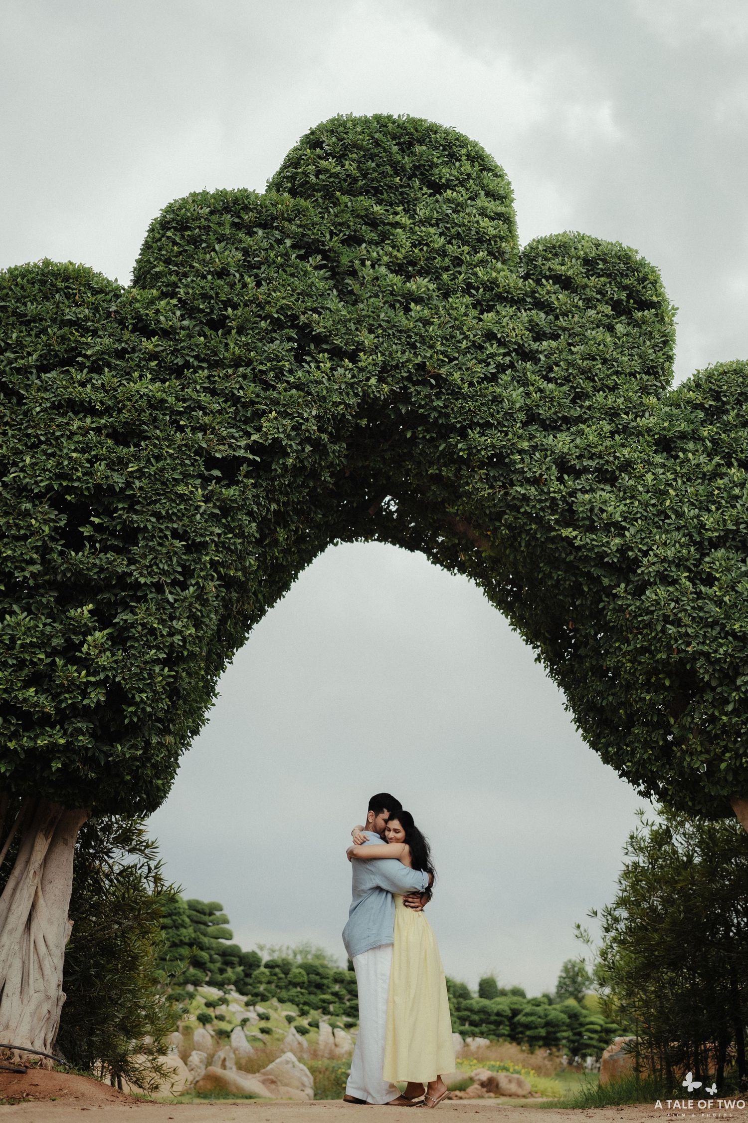 A scenic garden archway formed by manicured trees frames a couple sharing a romantic moment.