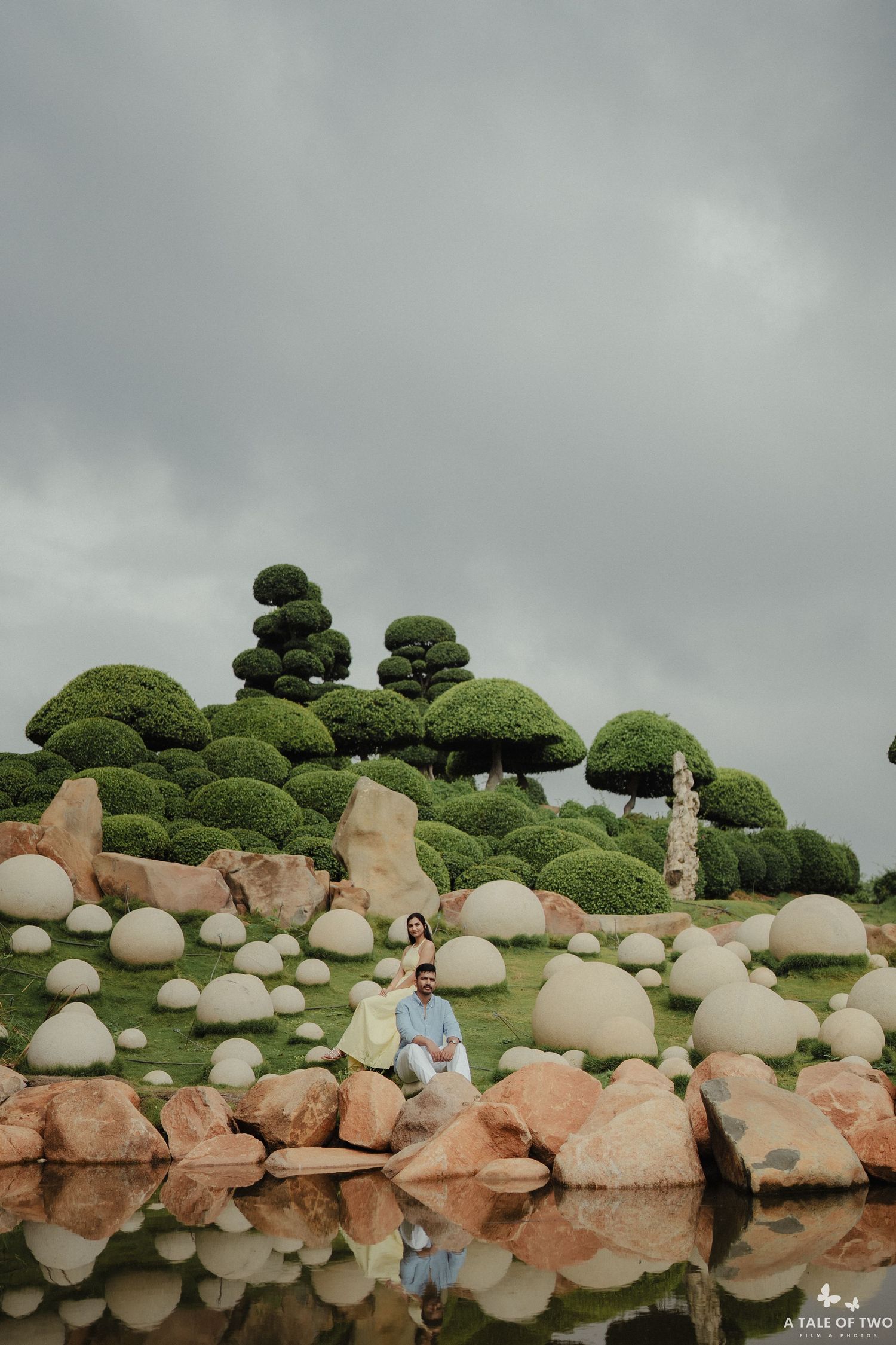 Scenic landscape with mossy green trees and round rocks reflecting in still water under cloudy skies.