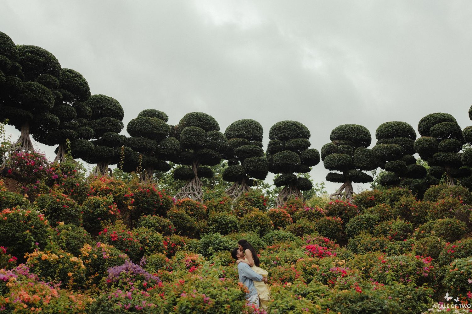 Artistically pruned topiary trees line a garden path filled with colorful flowering bushes and plants.
