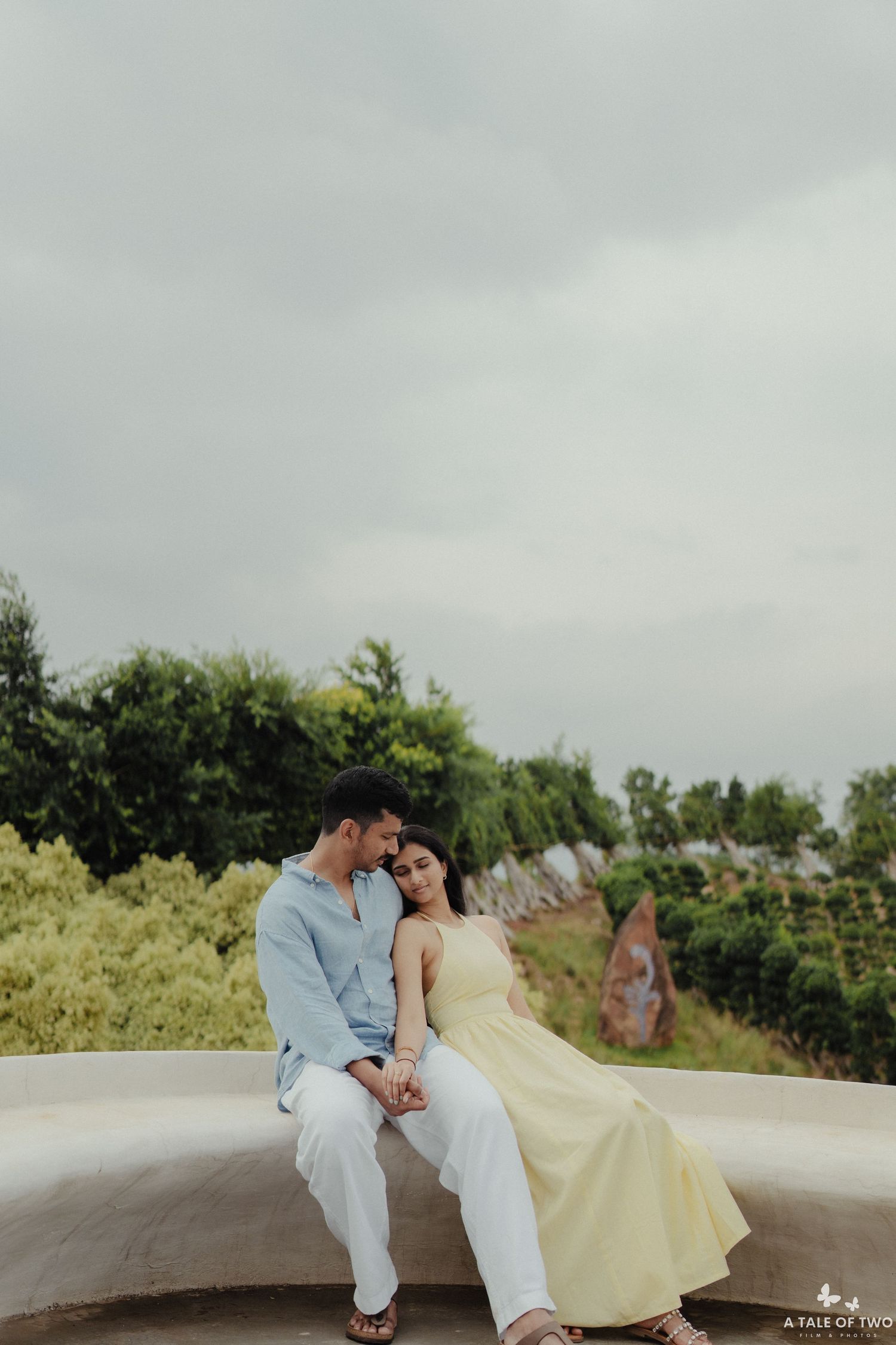 A couple in white and yellow outfits share an intimate moment on a curved concrete structure outdoors.