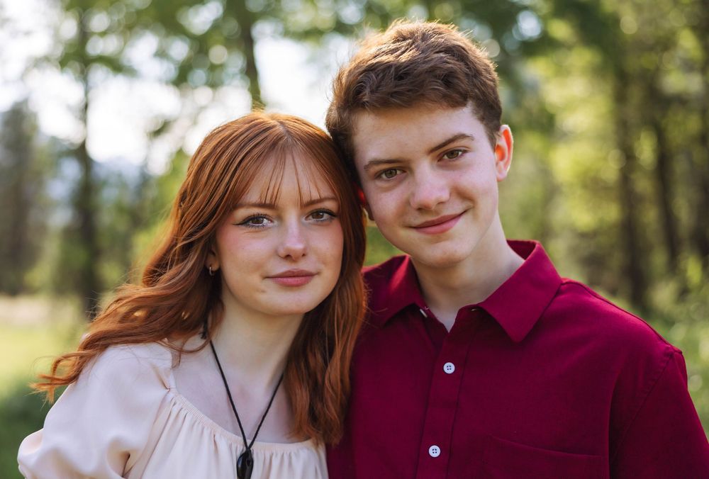 A couple poses together outdoors wearing burgundy and cream colored clothing.