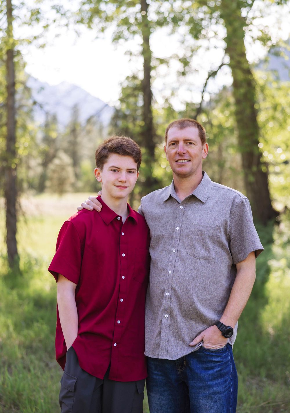 Three people stand together for a family portrait in a wooded outdoor setting.