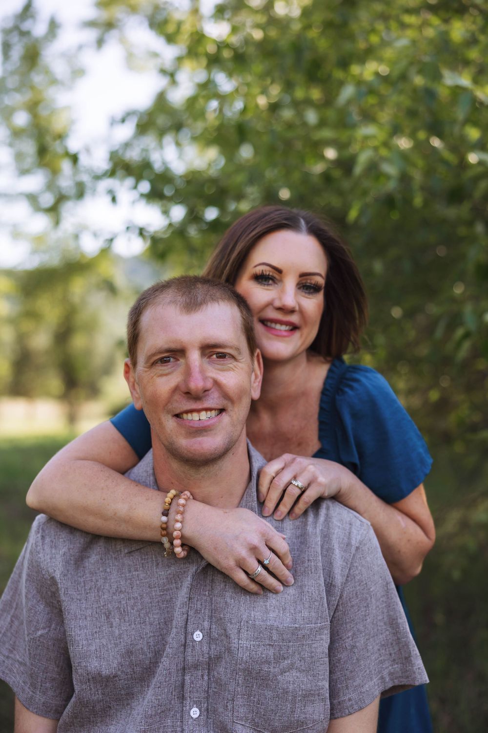 A couple shares a tender moment outdoors with natural greenery in the background.