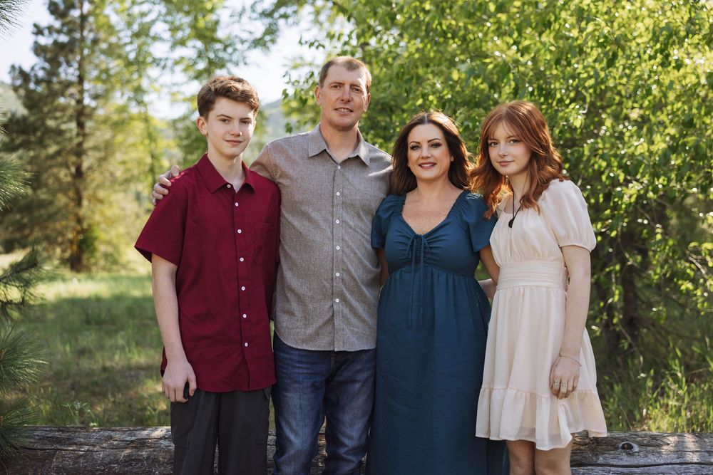 A family group poses together outdoors wearing coordinated casual attire.