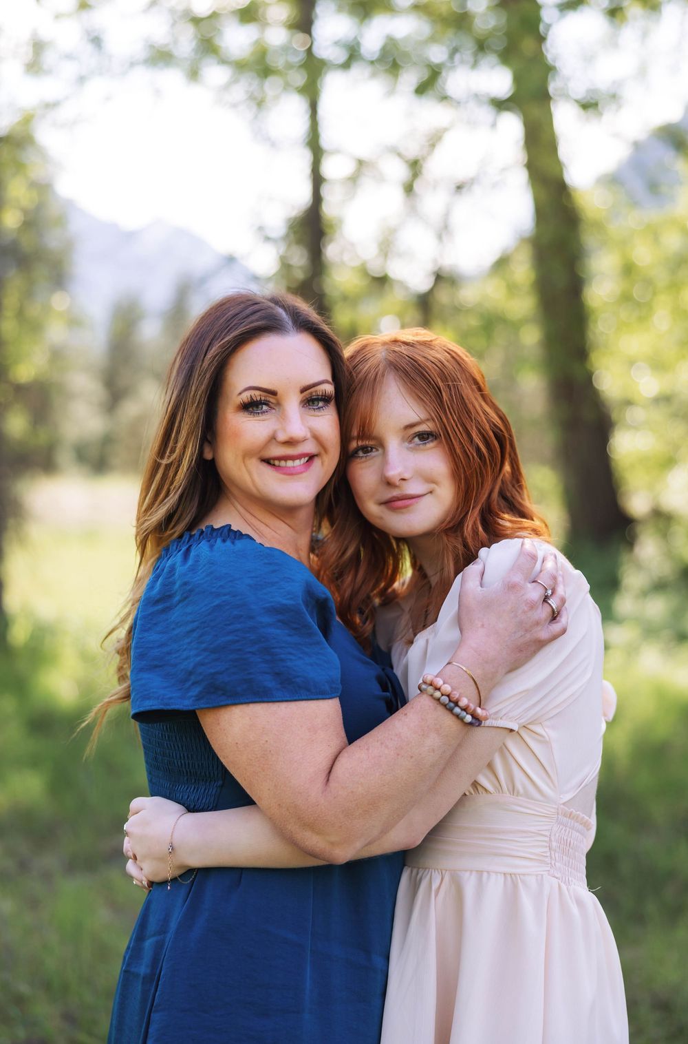 Two people share a warm embrace while standing in a sunlit outdoor setting.