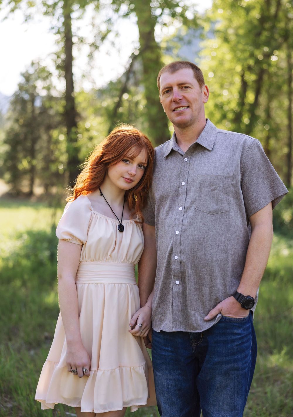 A couple poses casually together outdoors wearing grey and cream colored clothing.