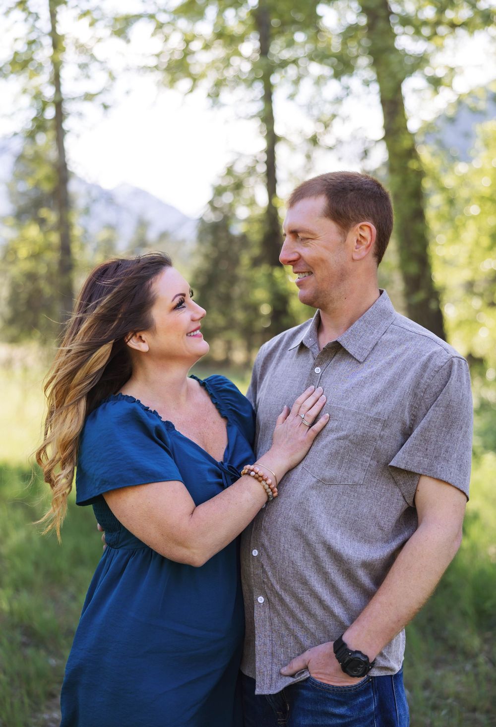 Playful couple laughing together during an outdoor photo session with trees in the background.