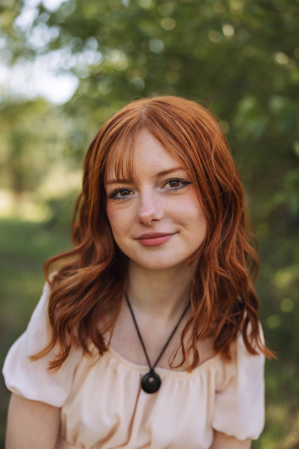 Portrait series of someone with red hair wearing a cream colored top and pendant necklace.