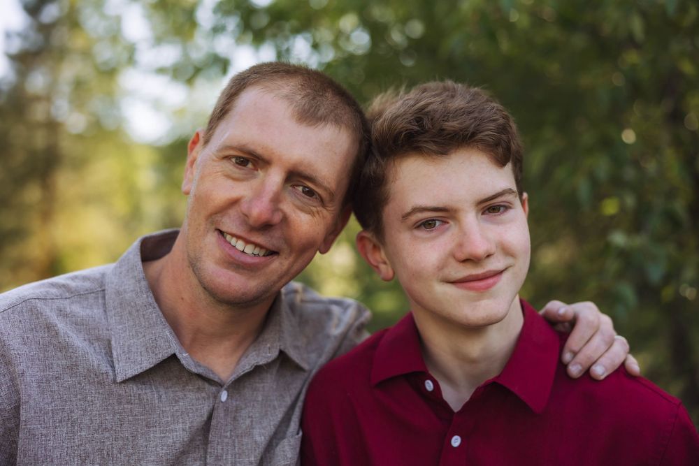Two people share warm embraces and smiles in an outdoor family photo series.