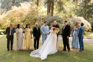 Wedding party members stand together in a line on a lush green lawn during a sunny autumn day.