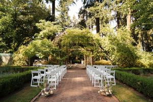 Peaceful garden wedding ceremony setup with rows of white chairs lining a shaded path between manicured hedges.